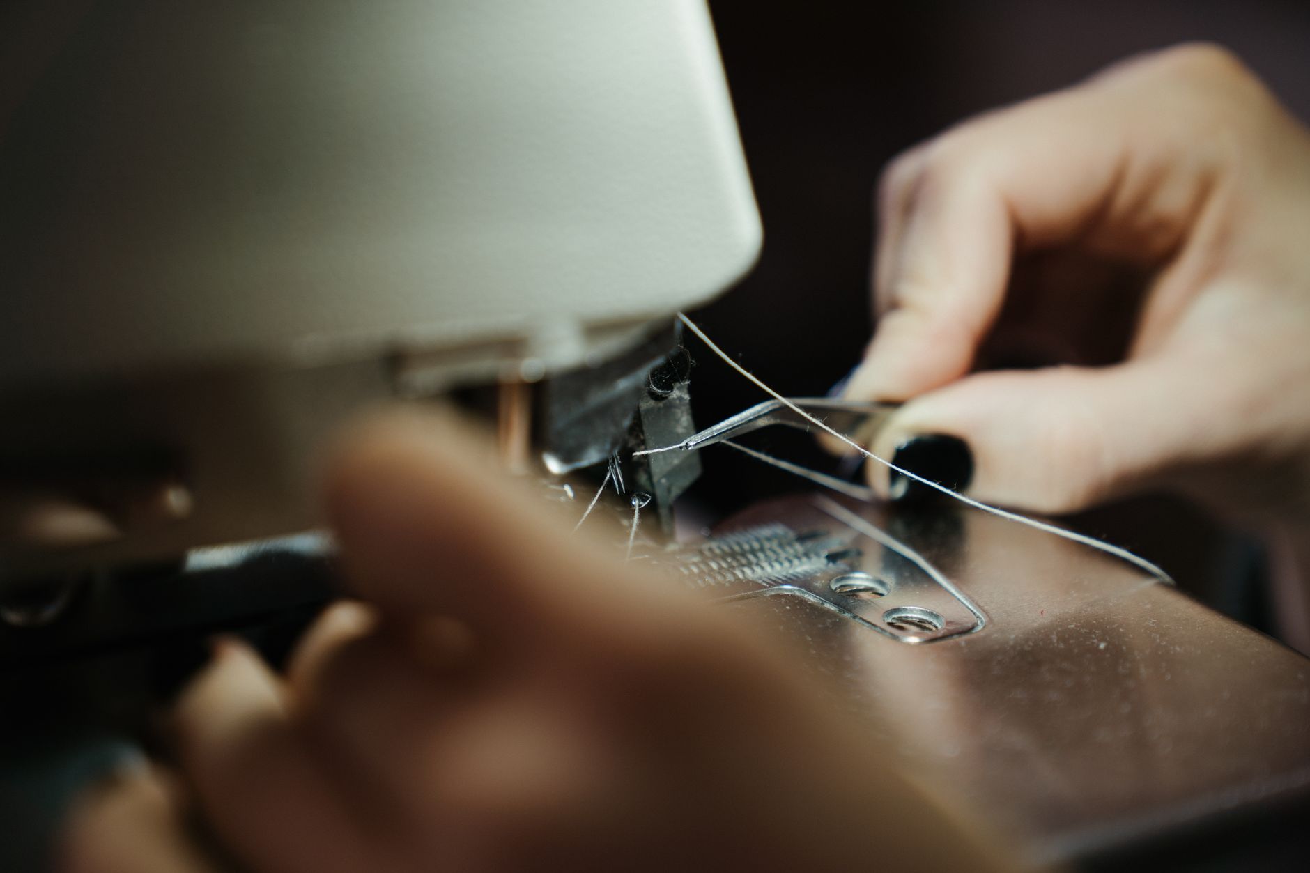 Hands threading a sewing machine in the HAUL workshop